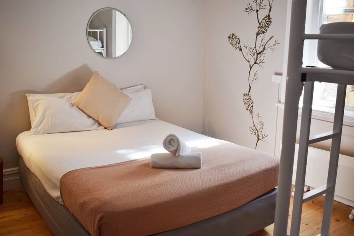 A neatly made bed with a brown blanket, white pillows, and a rolled towel. A mirror hangs on the wall above the bed, and a decorative wall piece is visible to the right.