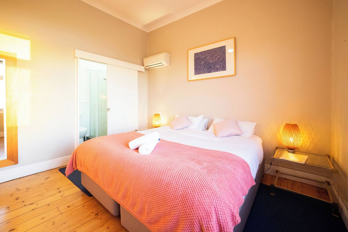 A bedroom with a bed, a bedside table, a lamp, an air conditioner, and a door.