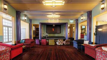 A spacious lobby with a large flat-screen TV, multiple patterned sofas, and a wooden floor.