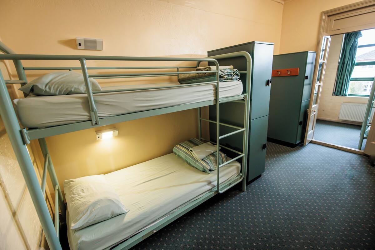 A bunk bed room with a radiator, a cabinet, and a window.