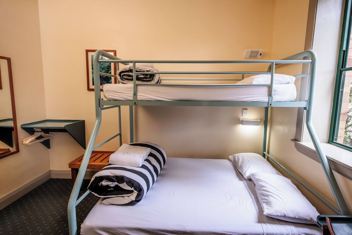 A bunk bed room with a wooden bench, a small table, and a mirror.