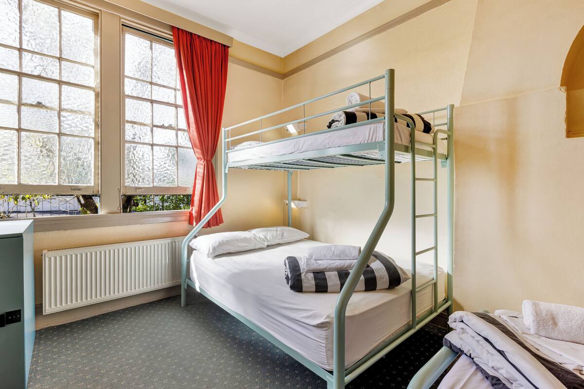 A bunk bed room with a window, radiator, and a desk.