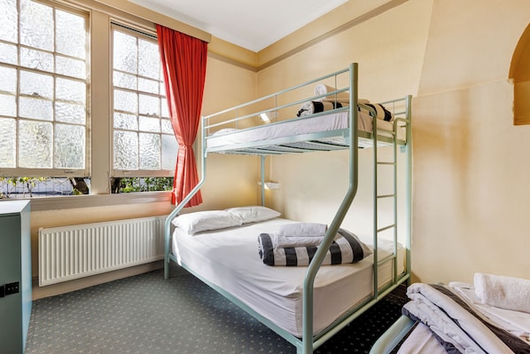 Dormitorio con literas, ventana, radiador y escritorio.