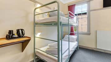 Een slaapkamer met een stapelbed, een houten plank met een koffiezetapparaat en bekertjes, een raam met gordijnen en een radiator.