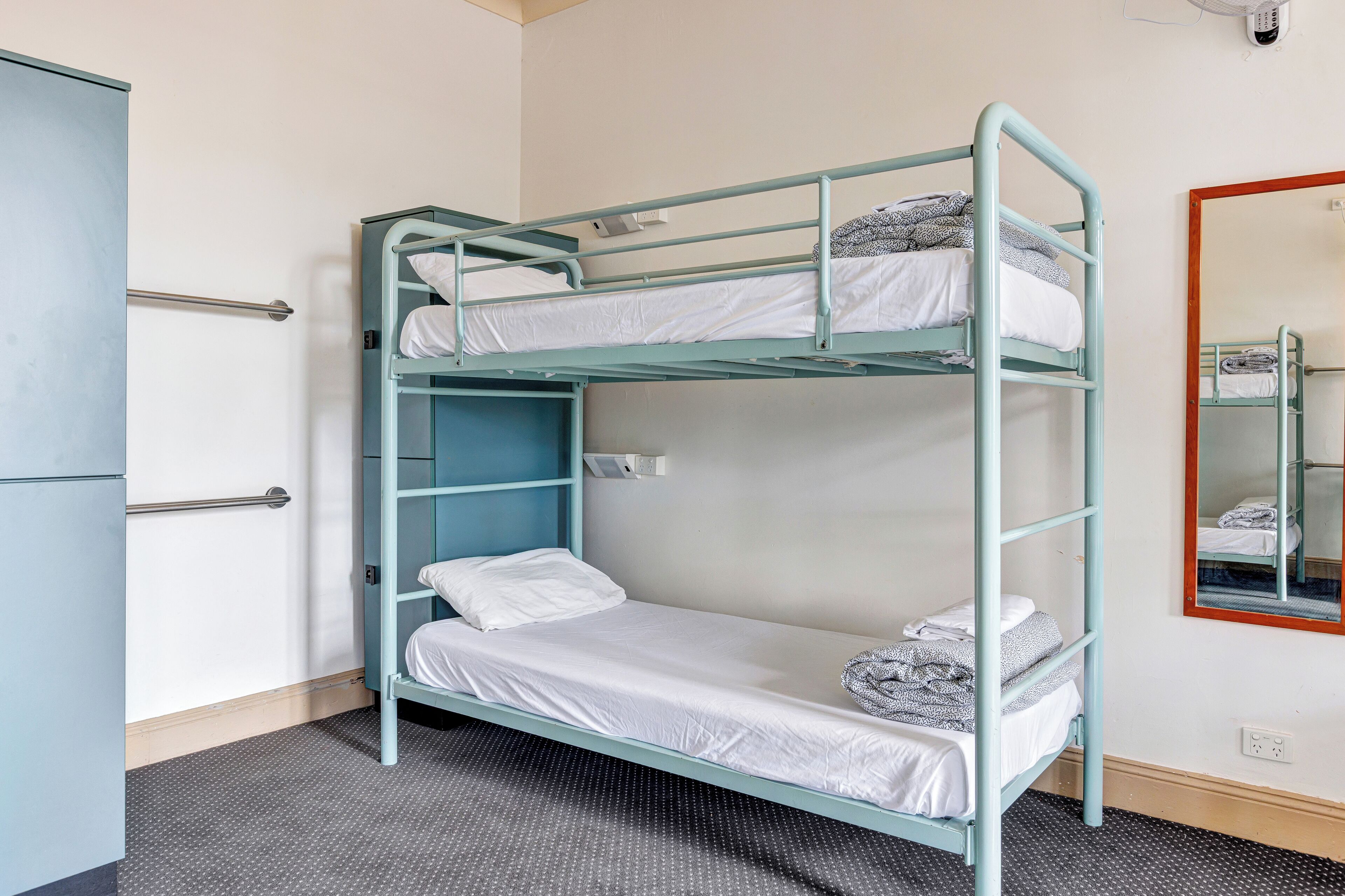 A bunk bed with a metal frame, a small shelf, and a mirror on the wall.
