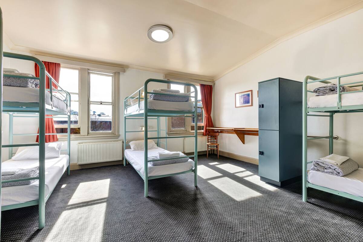 A dormitory room with bunk beds, a desk, and a radiator.