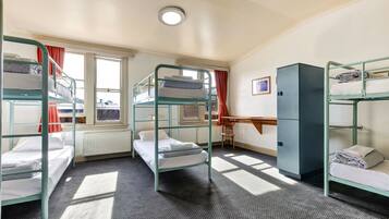 A dormitory room with bunk beds, a desk, and a radiator.
