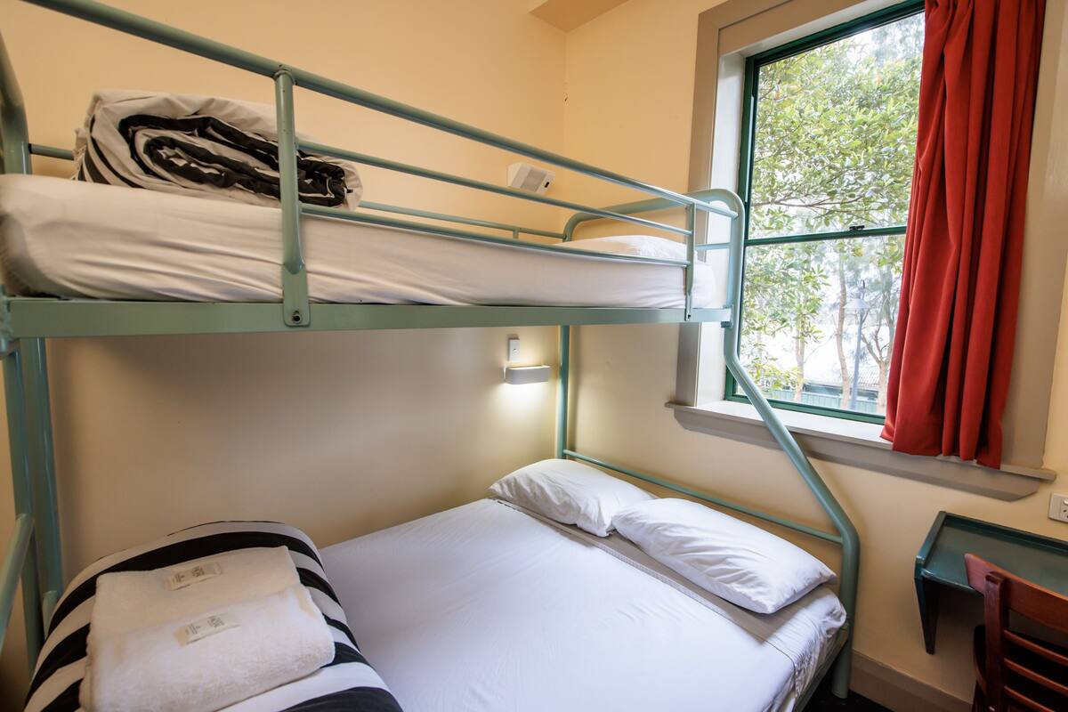 A bunk bed room with a window, a desk, and a chair.