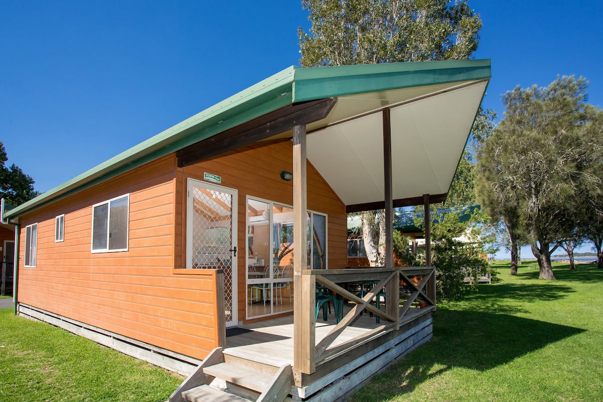 A wooden cabin with a covered porch, a glass door entrance, and a small outdoor seating area.