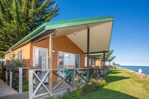 A wooden cabin with a covered deck, large windows, and a view of the sea.