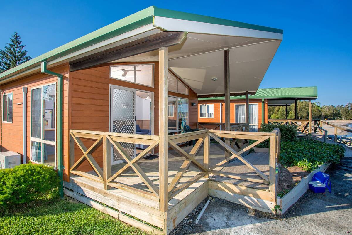 A wooden cabin with a covered porch, large windows, and a fenced garden area.