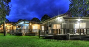 A row of cabins with outdoor decks and covered porches, surrounded by trees.