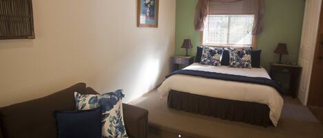 A bedroom with a bed, a nightstand, a lamp, a couch, and a wall-mounted picture.