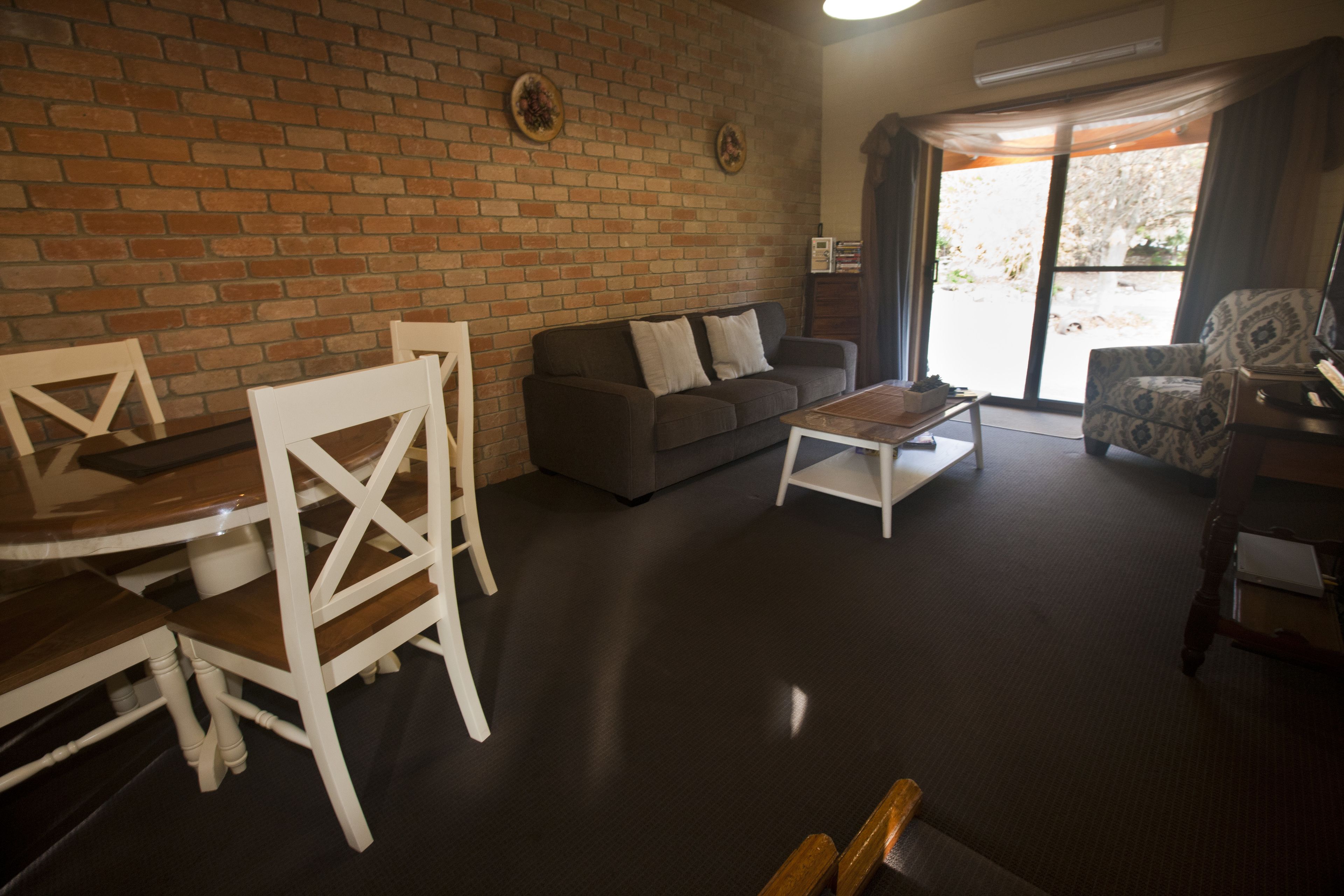 Una sala de estar con pared de ladrillo, un sofá, una mesa de centro y un sillón estampado.