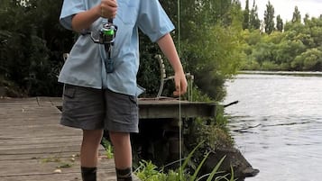 A person fishing on a wooden dock by a calm river, surrounded by greenery.