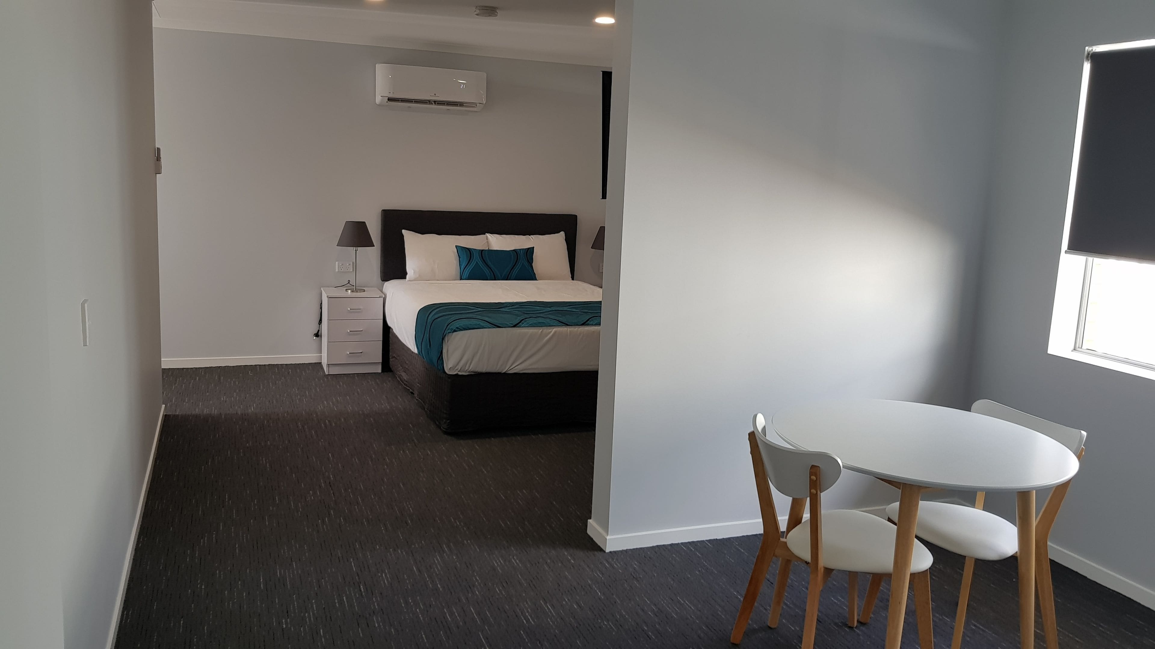 A modern bedroom with a bed, bedside table, lamp, and a small table with chairs.