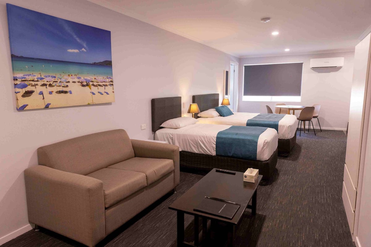 A hotel room with a bed, a sofa, a desk, and a painting of a beach scene.