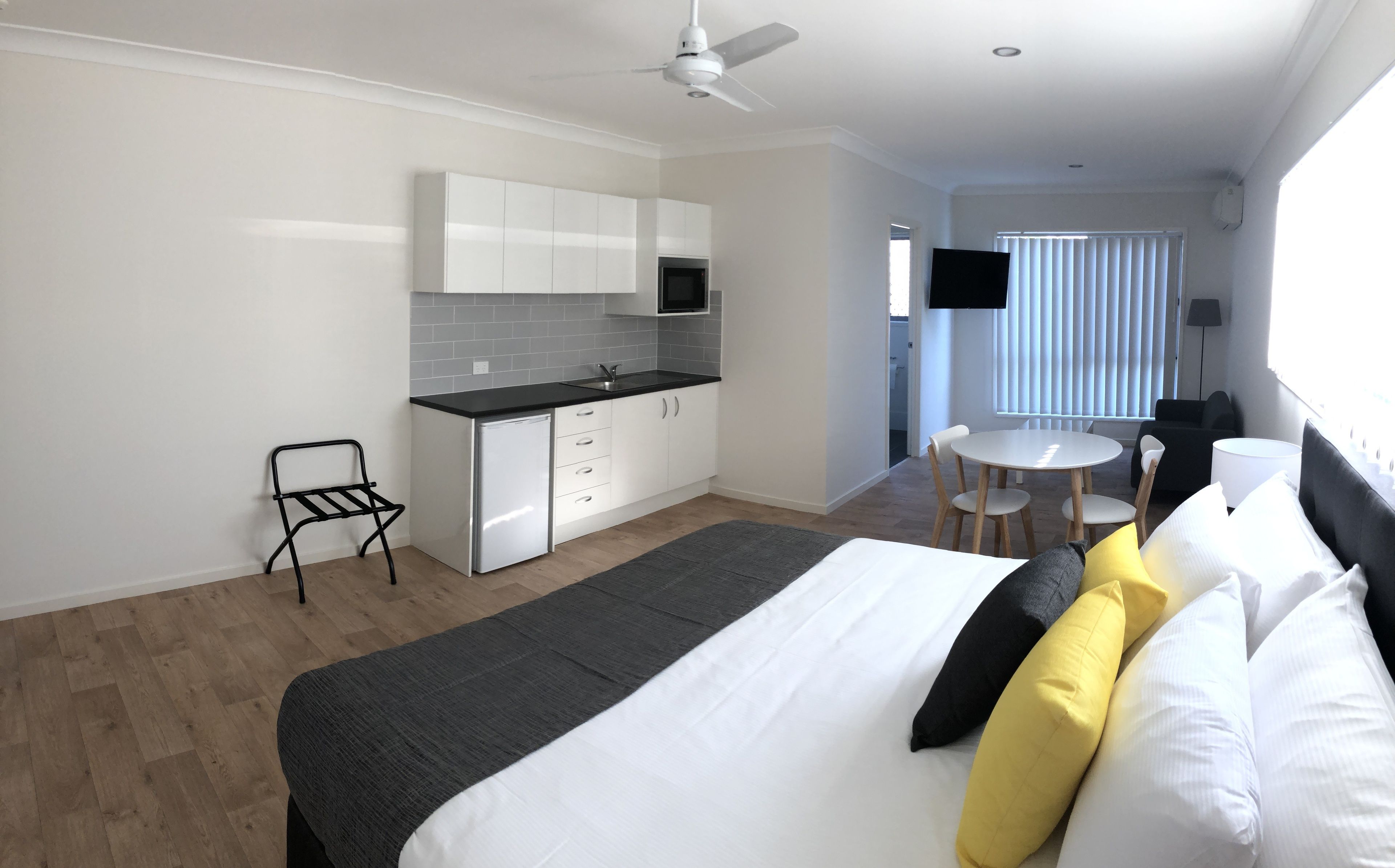 Quarto de hotel moderno com cama, pequena cozinha, área de refeições e televisão.