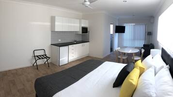 Quarto de hotel moderno com cama, pequena cozinha, área de refeições e televisão.