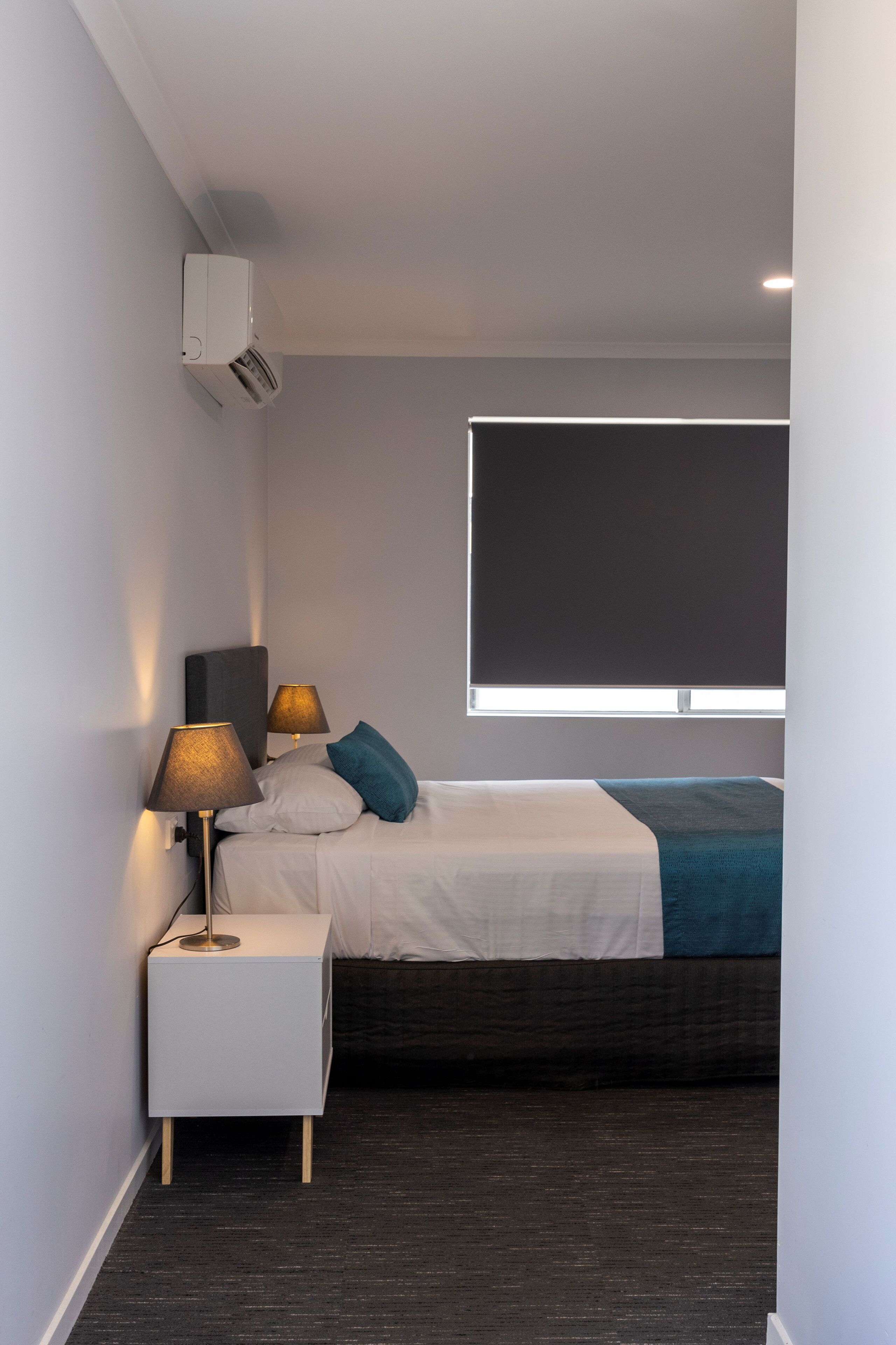 Un dormitorio moderno con cama, lámparas de noche, una ventana y un equipo de aire acondicionado.