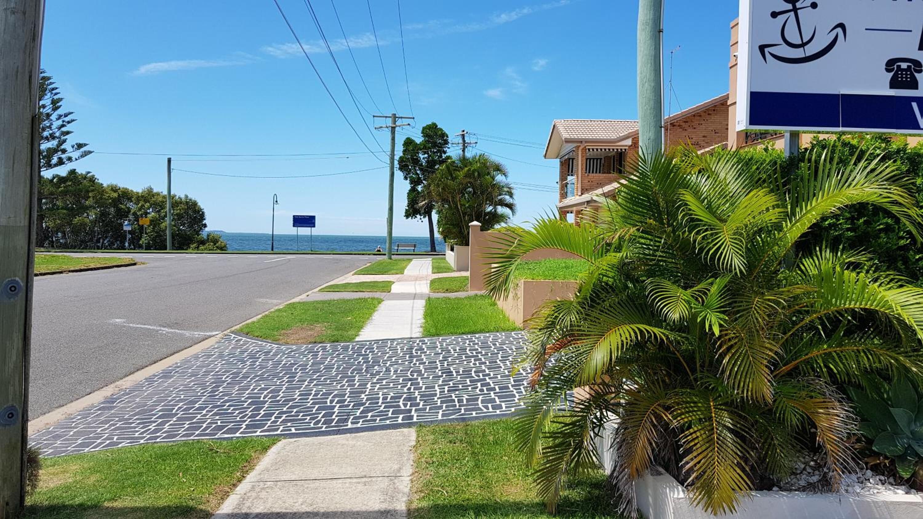 Una carretera costera con acera pavimentada, palmeras y vista al mar.