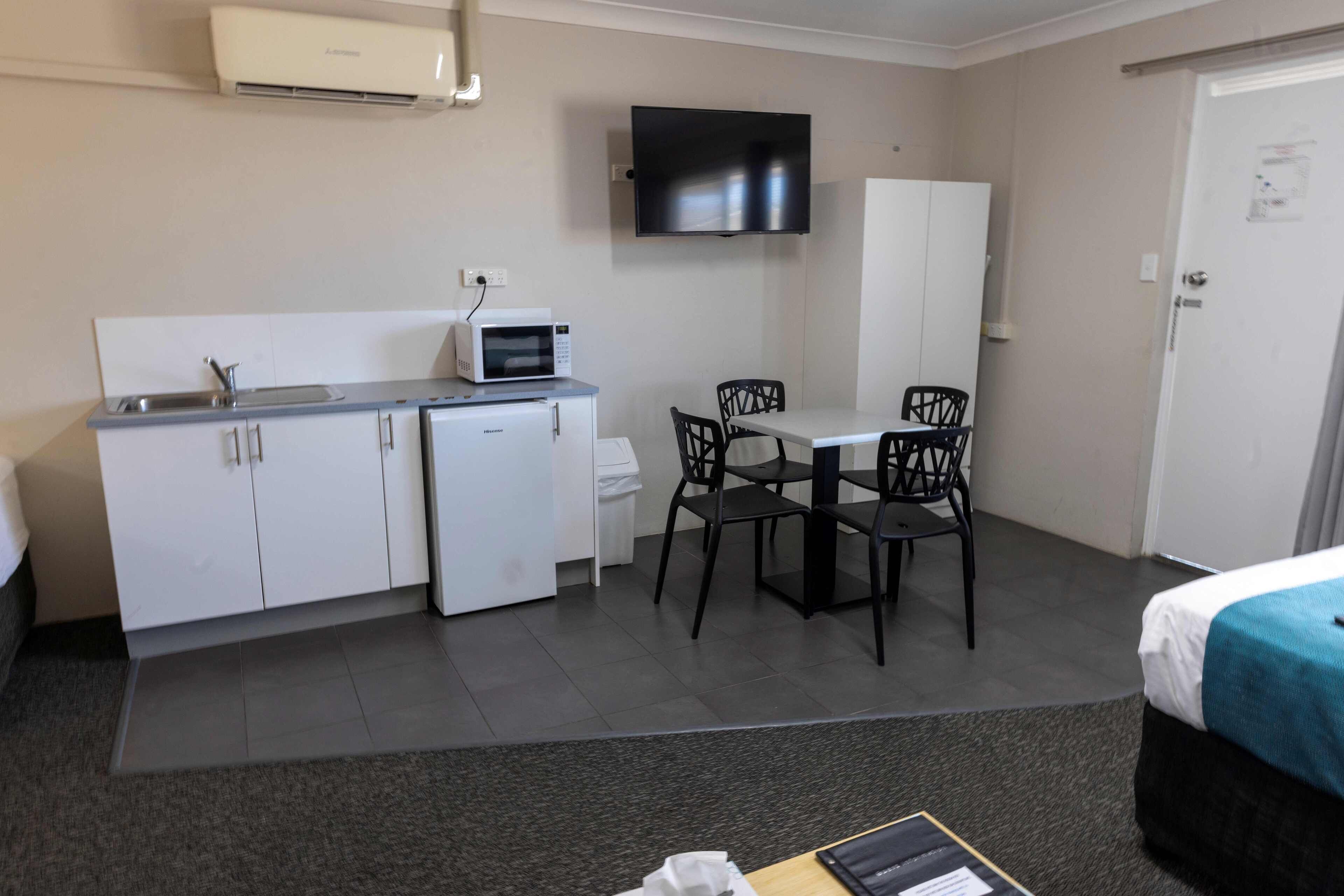 Habitación de hotel compacta con kitchenette, televisor de pantalla plana, cama y un pequeño comedor.