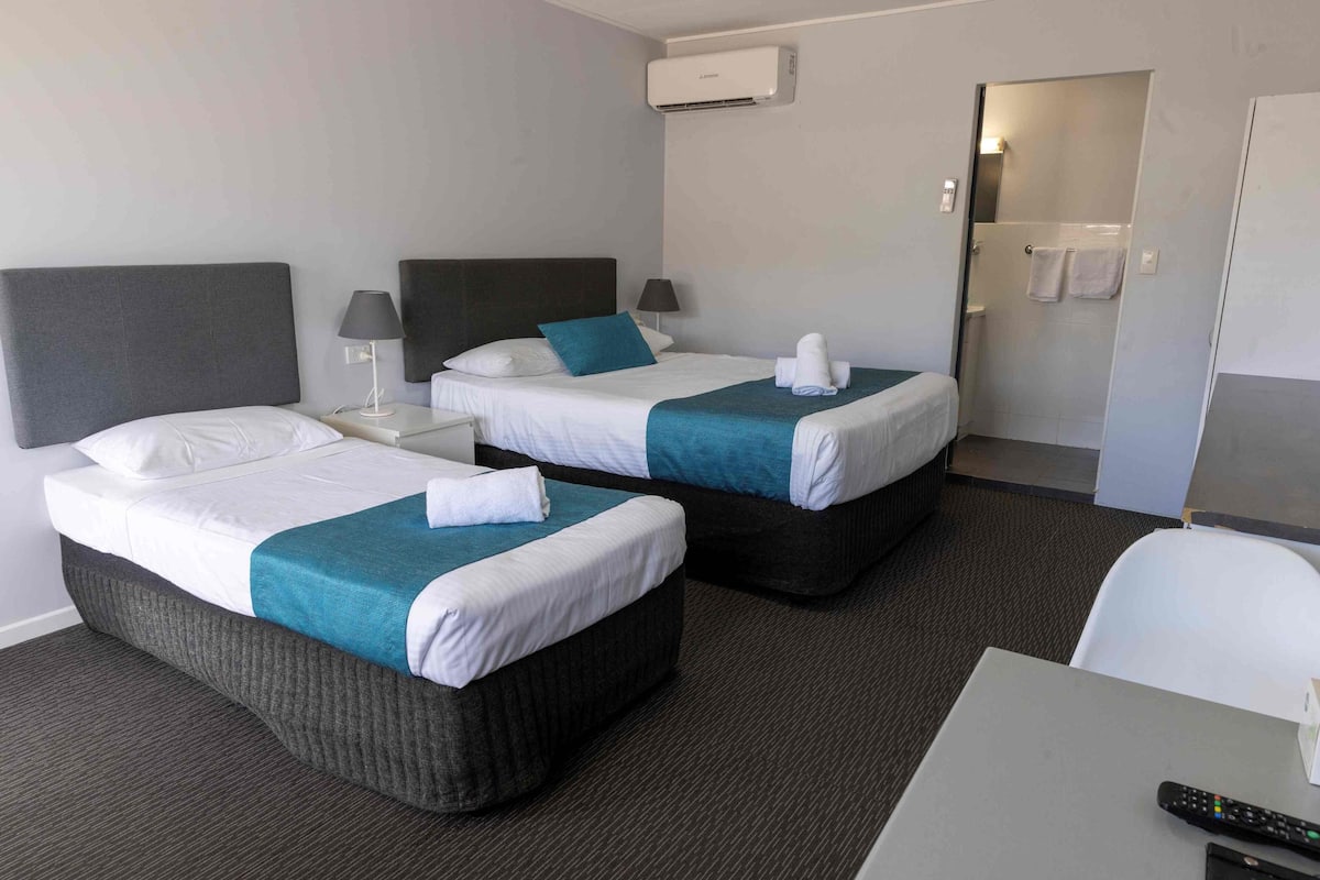 A hotel room with two beds, a desk, a chair, and a bathroom visible through an open door.