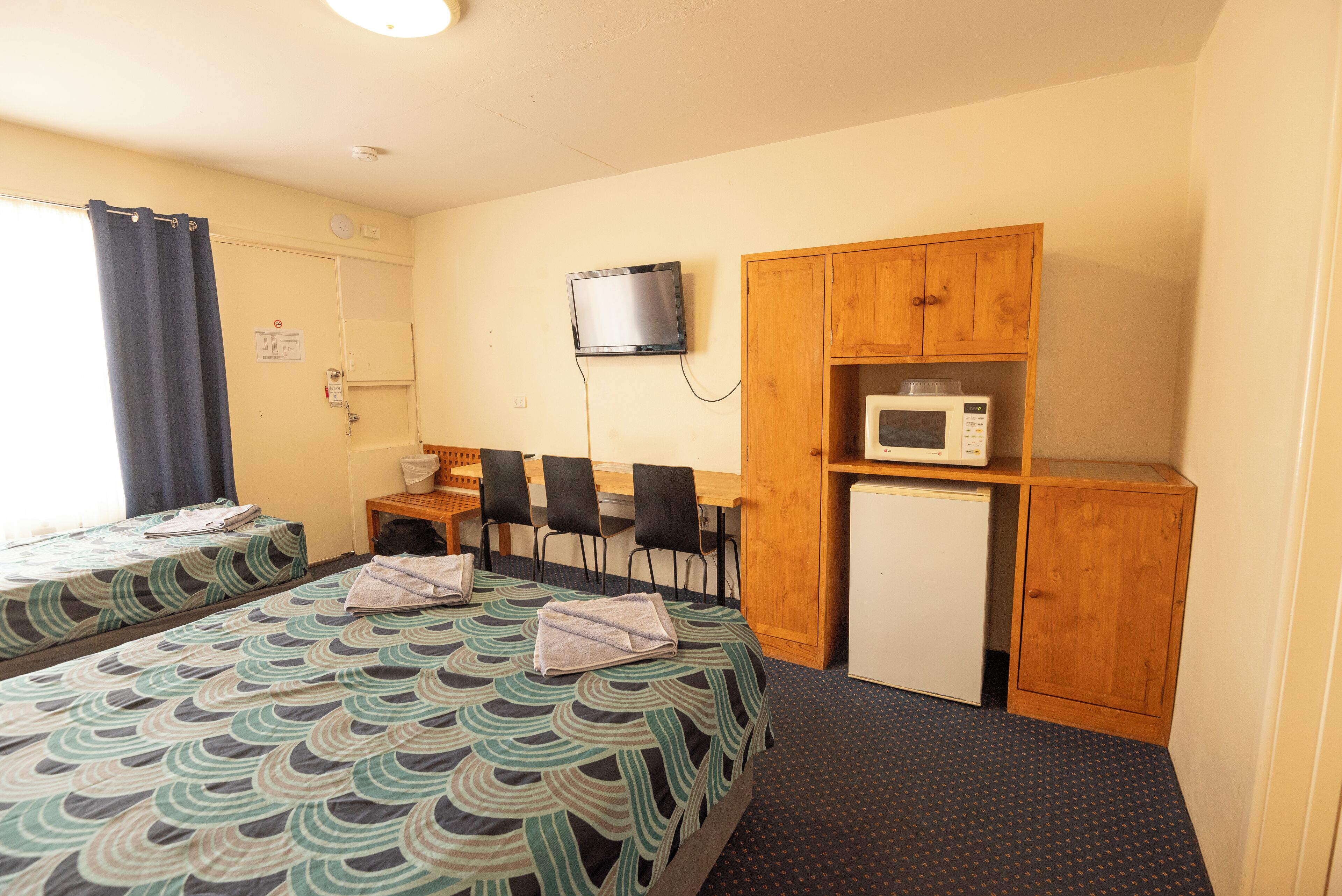 A hotel room with two beds, a desk, a television, a microwave, and a small refrigerator.
