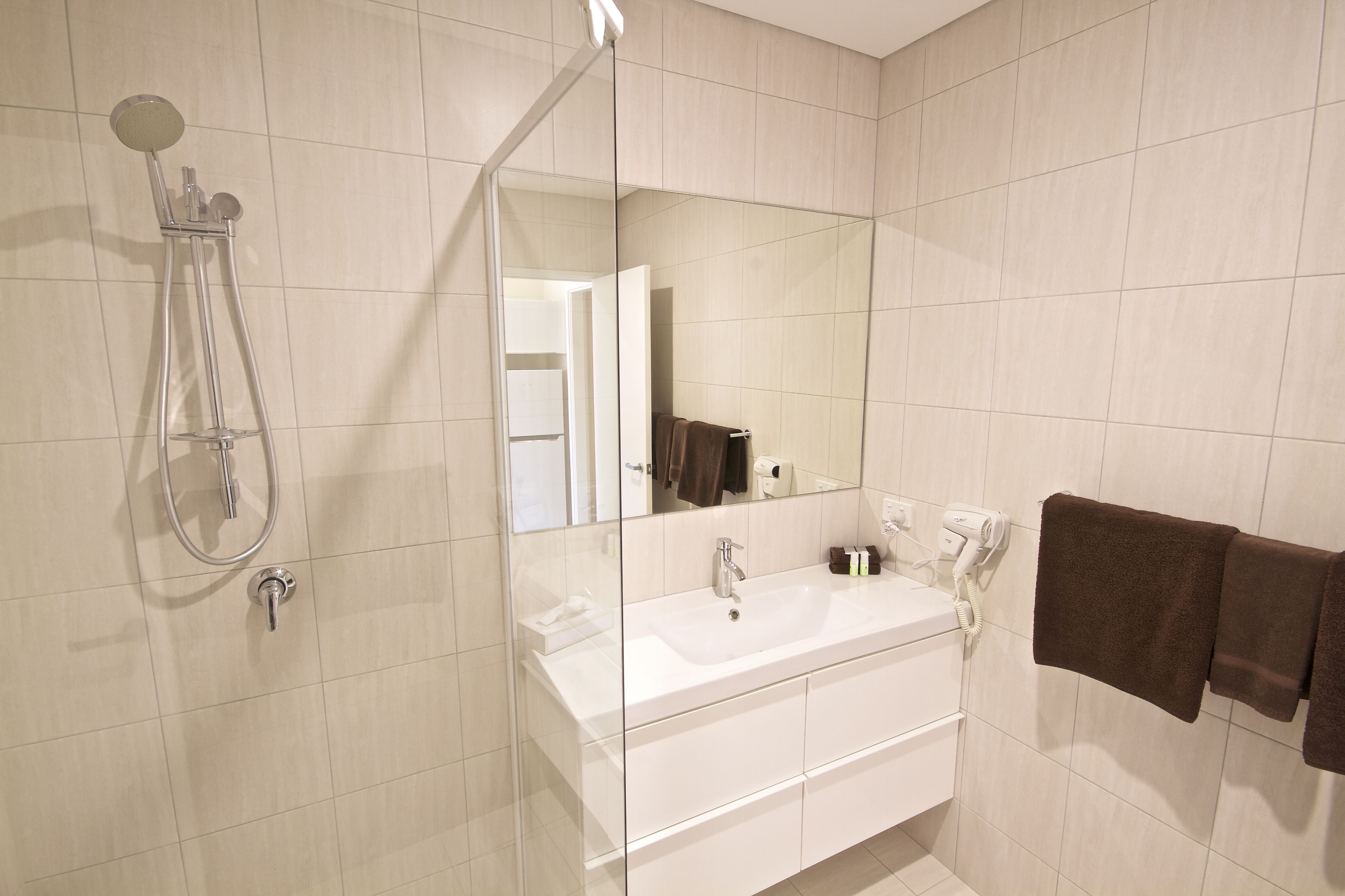 Un baño moderno con ducha envuelta en vidrio, un lavamanos blanco y un espejo grande.