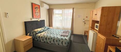 A hotel room with a bed, bedside table, wardrobe, and a small desk with a chair.