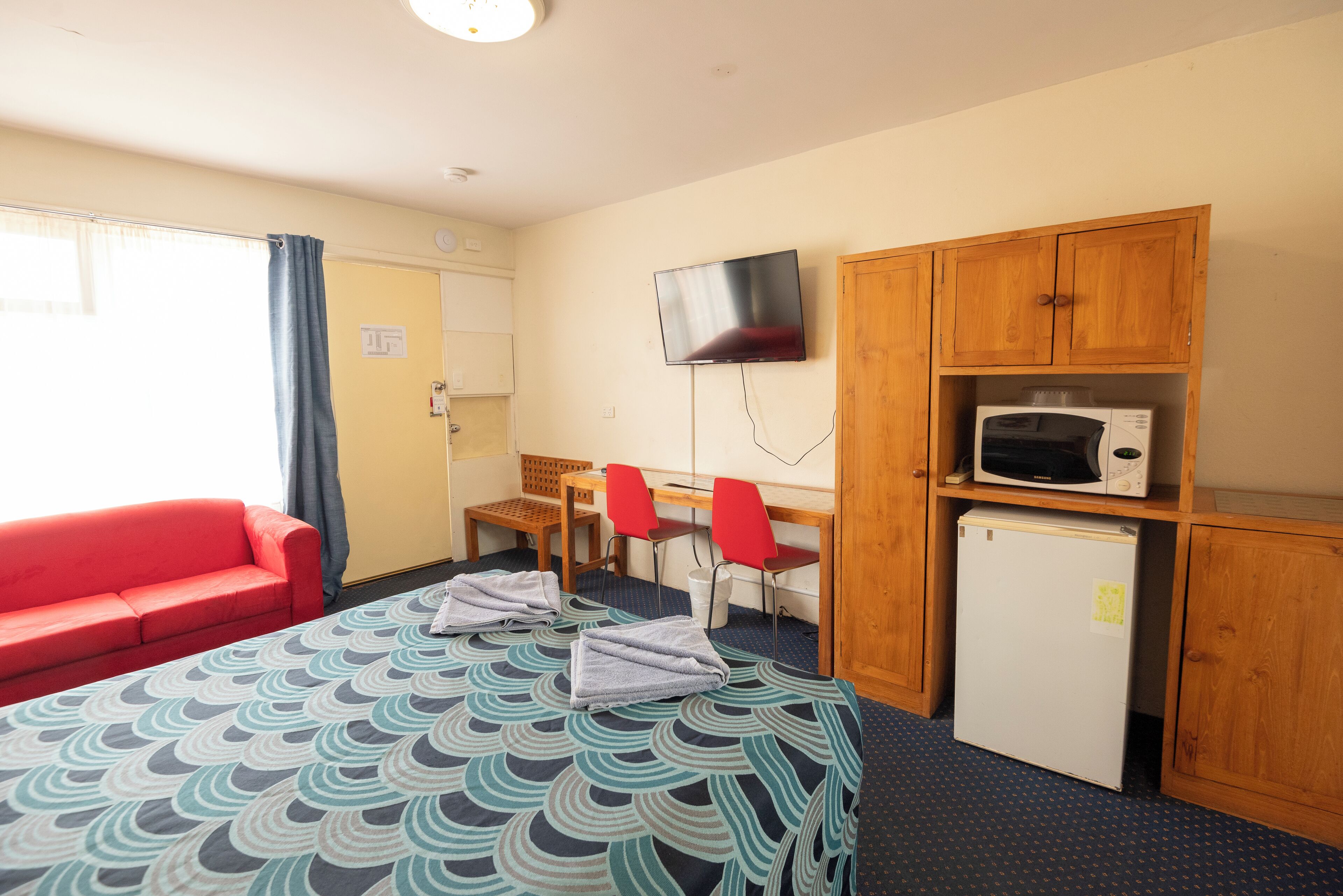 Hotelkamer met een bed, een rode bank, een bureau met twee stoelen, een televisie, een magnetron en een koelkast.