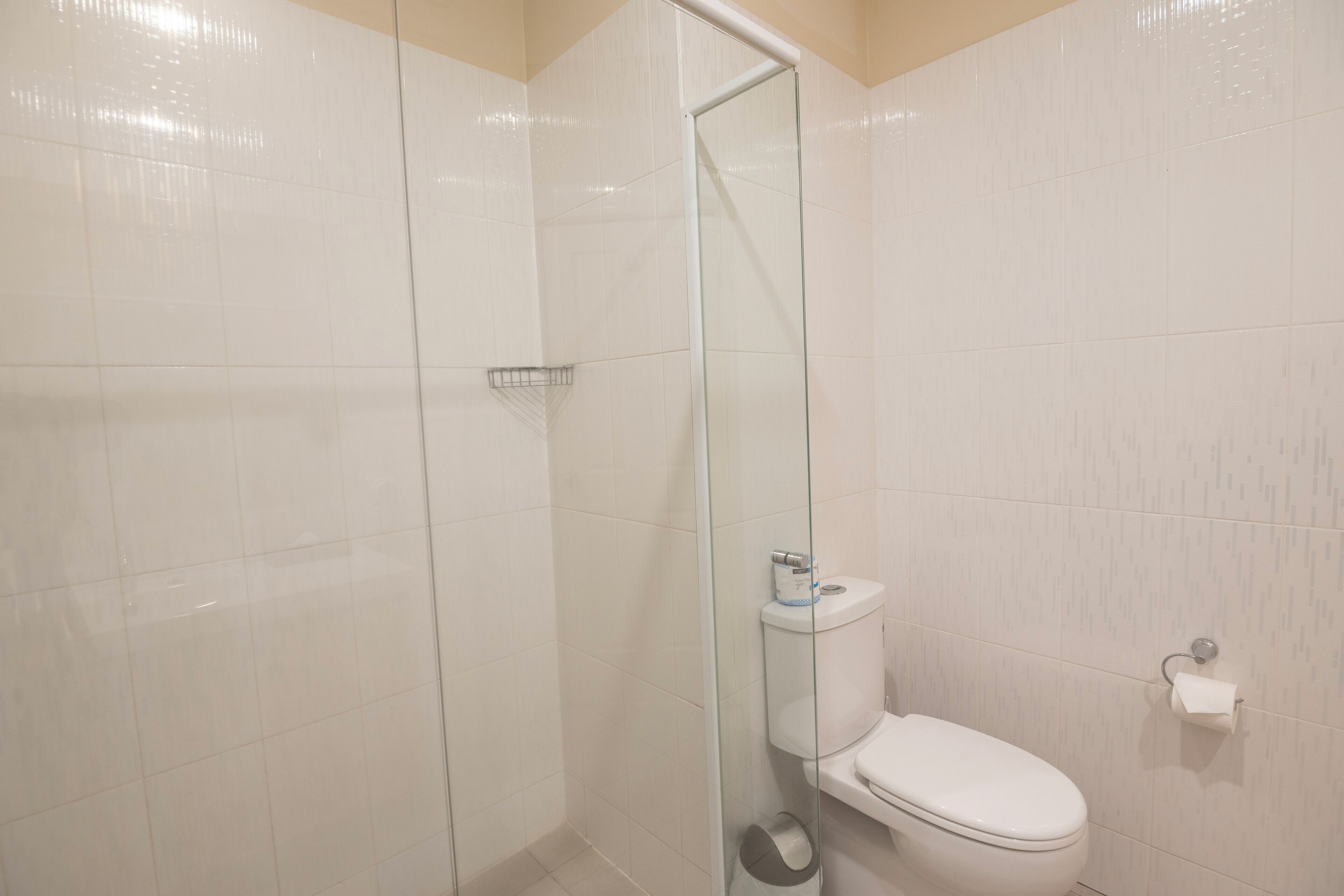 A bathroom with a glass shower enclosure, a toilet, and a paper towel holder.