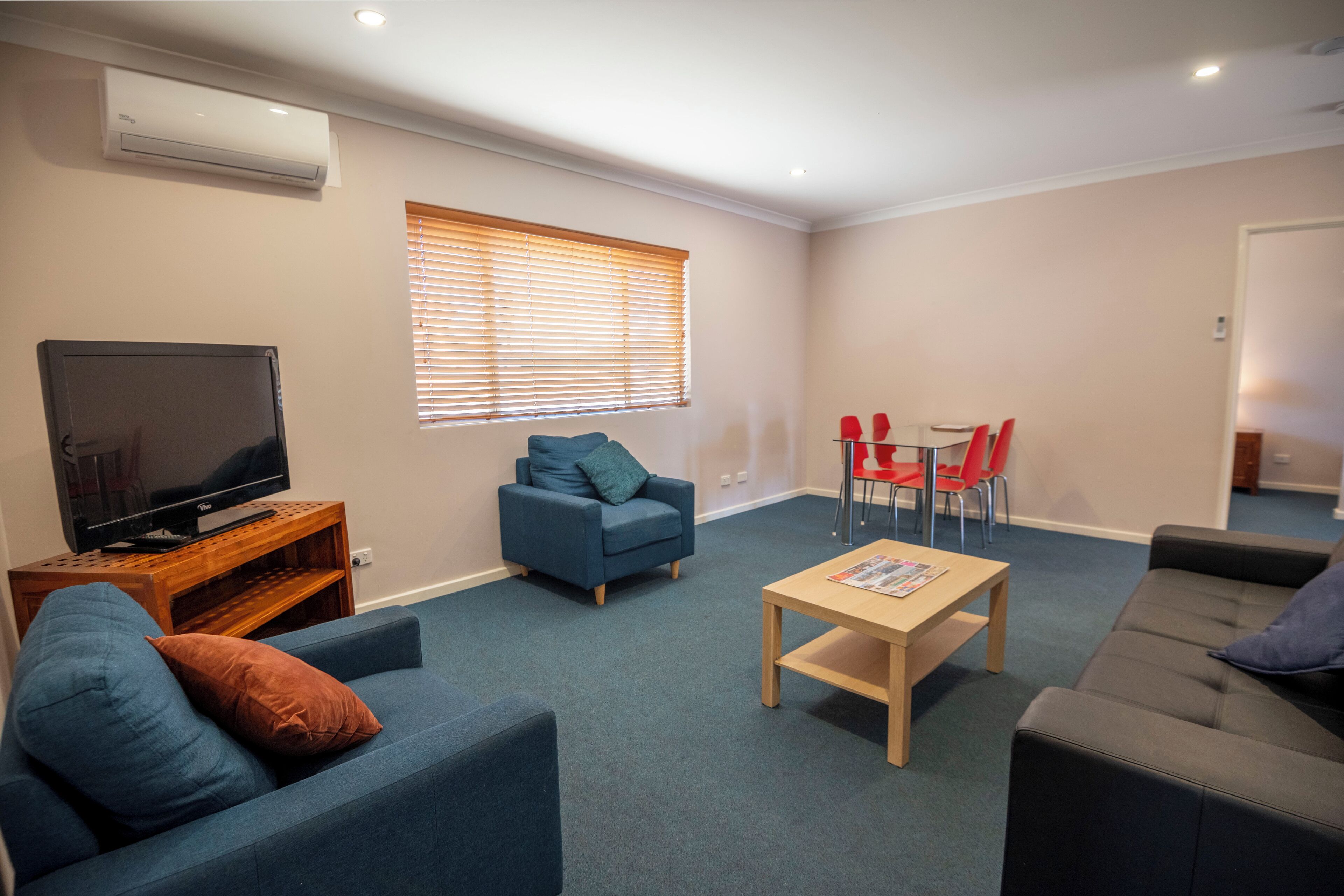 A living room with a television, sofas, a coffee table, and a dining area with chairs.