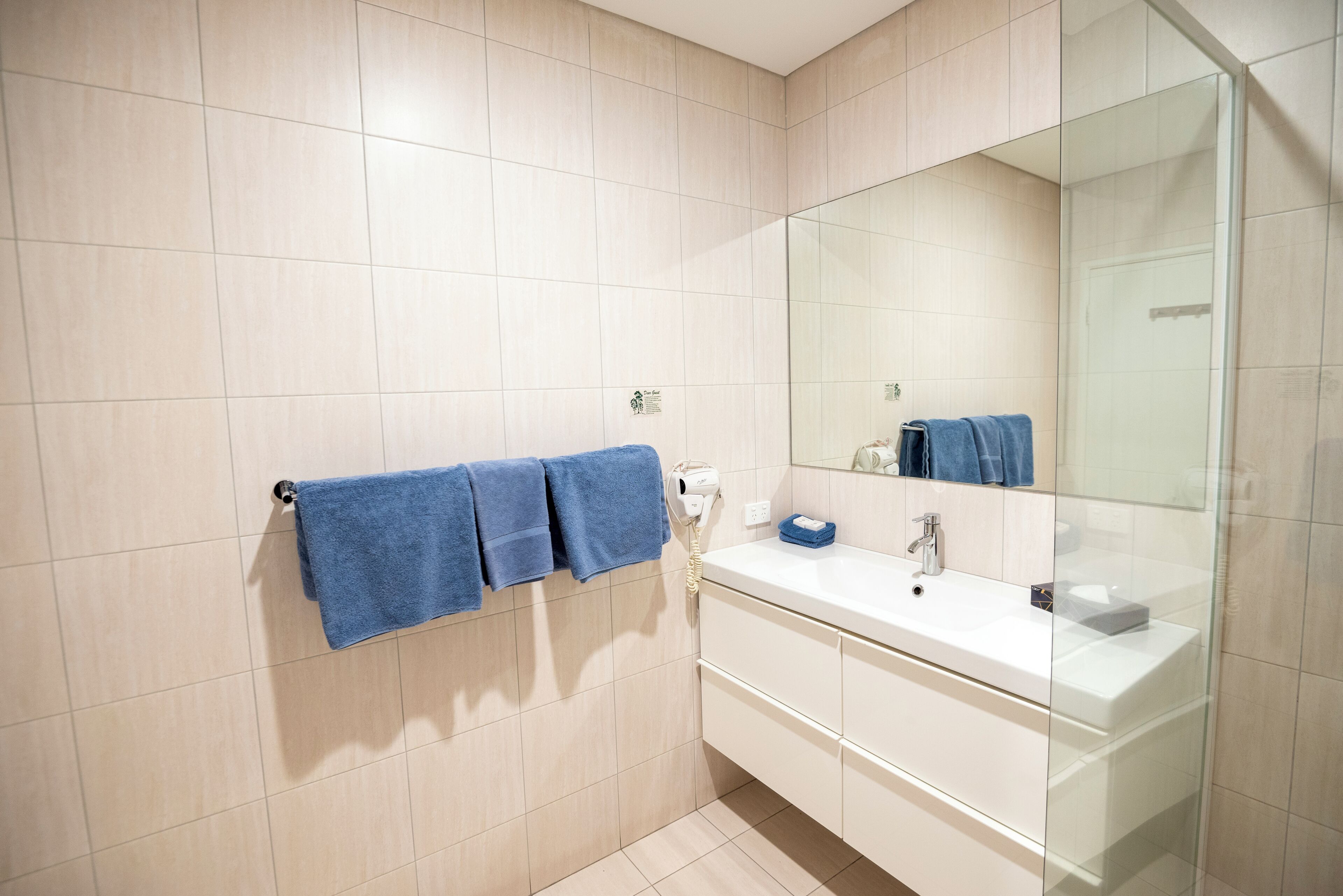 A bathroom with a white sink, a mirror, and three towels hanging on a towel rack.
