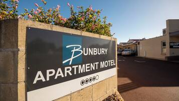 Cartel de Bunbury Apartment Motel, con vista despejada a la calle y automóviles estacionados al fondo.