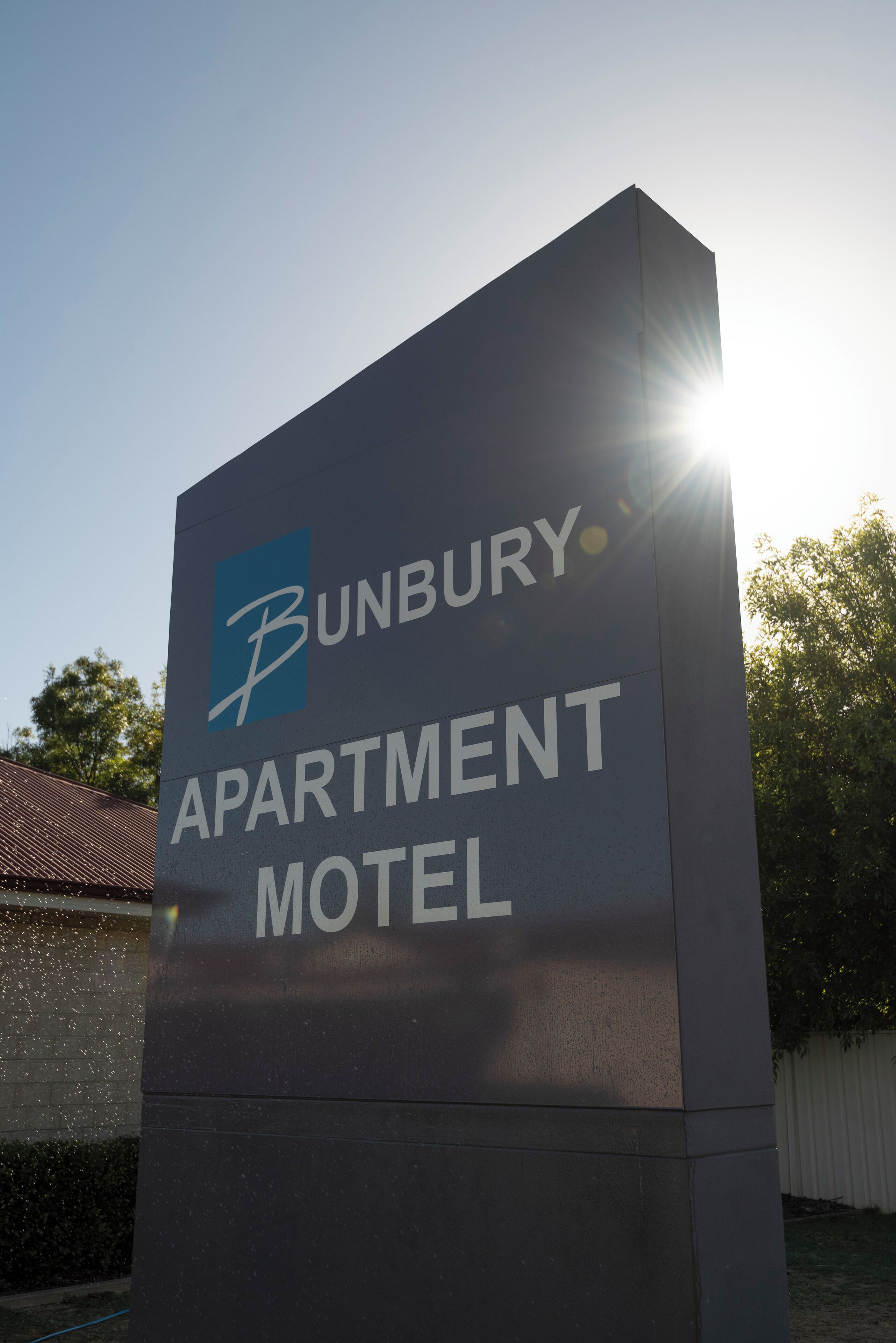 Cartel de Bunbury Apartment Motel con cielo despejado y luz solar al fondo.