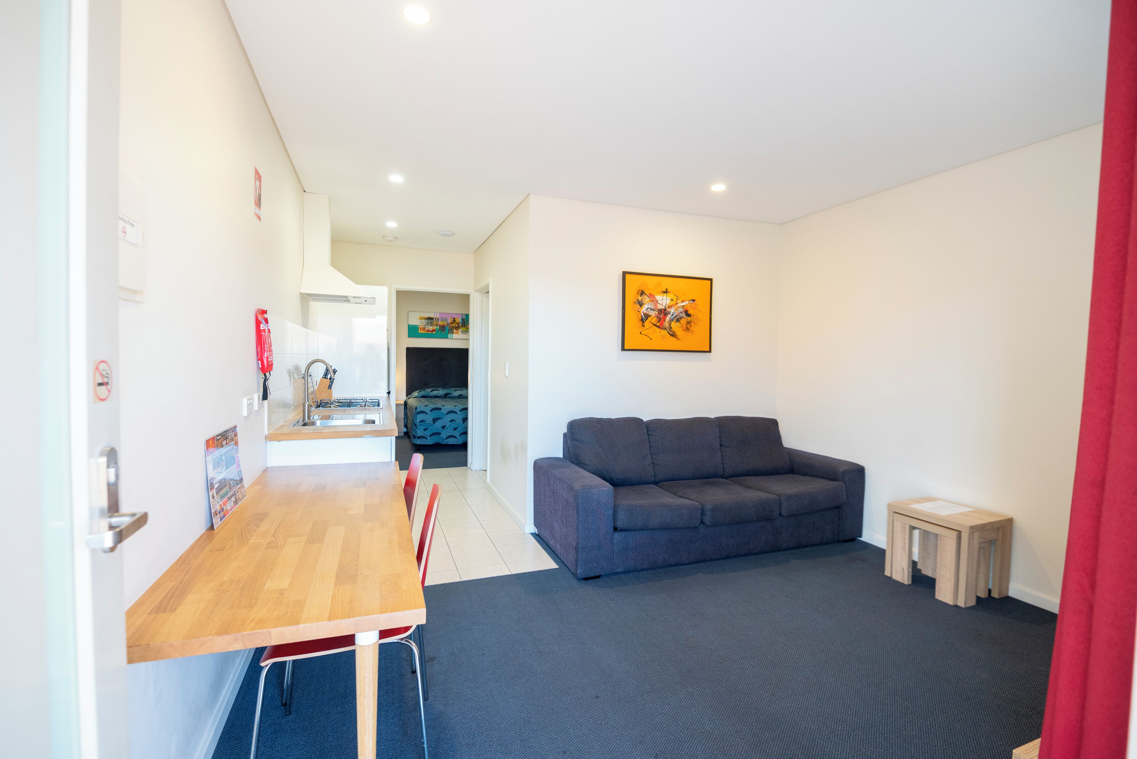 Una sala moderna con un sofá gris, una mesa de comedor de madera con sillas, un taburete de madera y un cuadro en la pared.