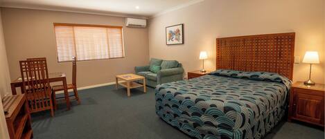 A bedroom with a bed, a desk, a chair, a small table, and a sofa.