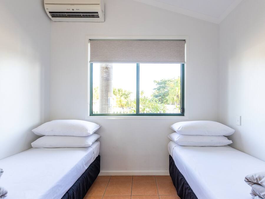 Una habitación con dos camas individuales, una ventana con vistas a zonas verdes y un equipo de aire acondicionado.