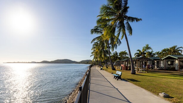 Een waterfrontpromenade met banken, palmbomen en een rij strandhutten.