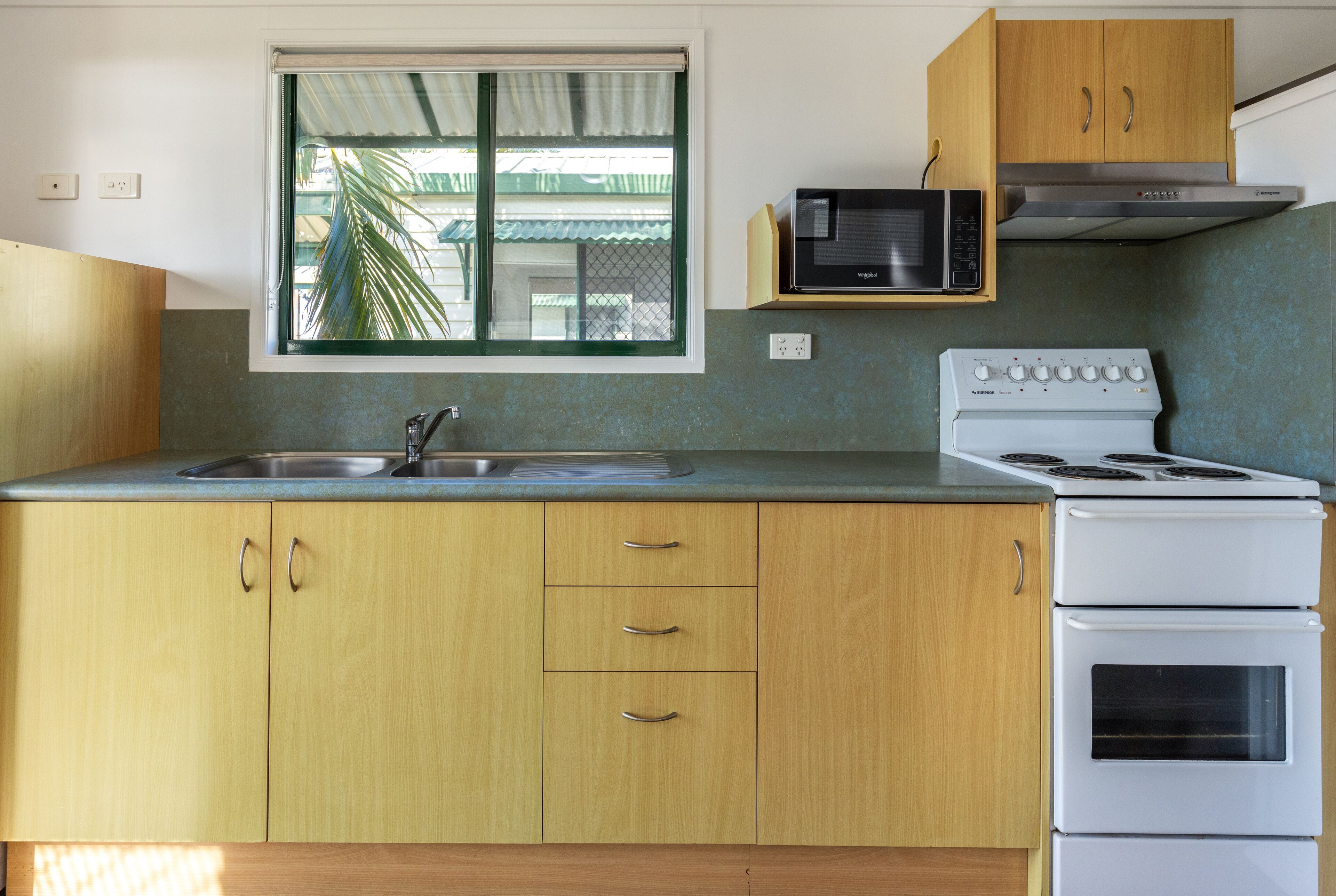 A kitchen with wooden cabinets, a microwave, a stove, and a window with a view of a building outside.