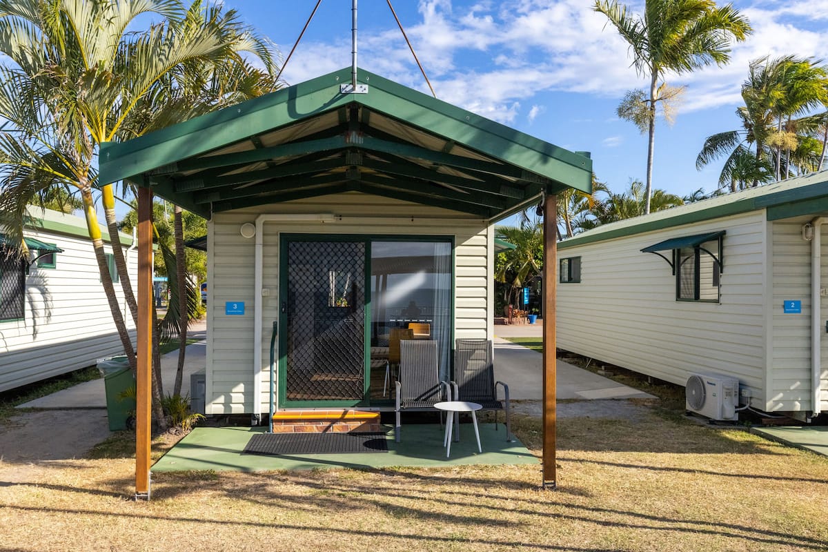 Une petite maison mobile d’un seul étage, dotée d’un auvent vert et d’une véranda grillagée. Un panneau indiquant le numéro « 3 » est affiché, ce qui correspond au numéro de l’unité.