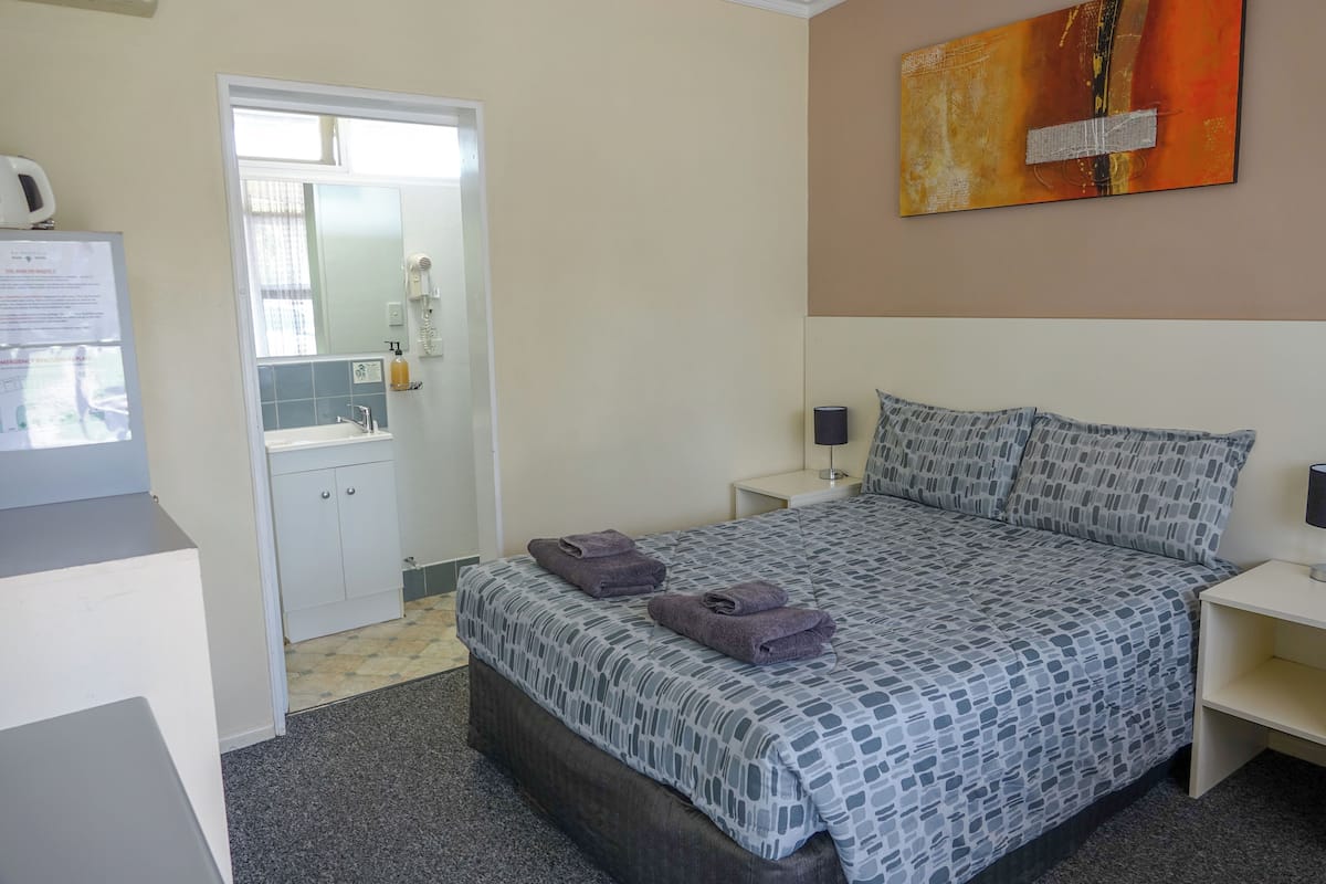 Une chambre à coucher comprenant un lit, des tables de chevet, une commode, un miroir, une porte et une œuvre d’art accrochée au mur.