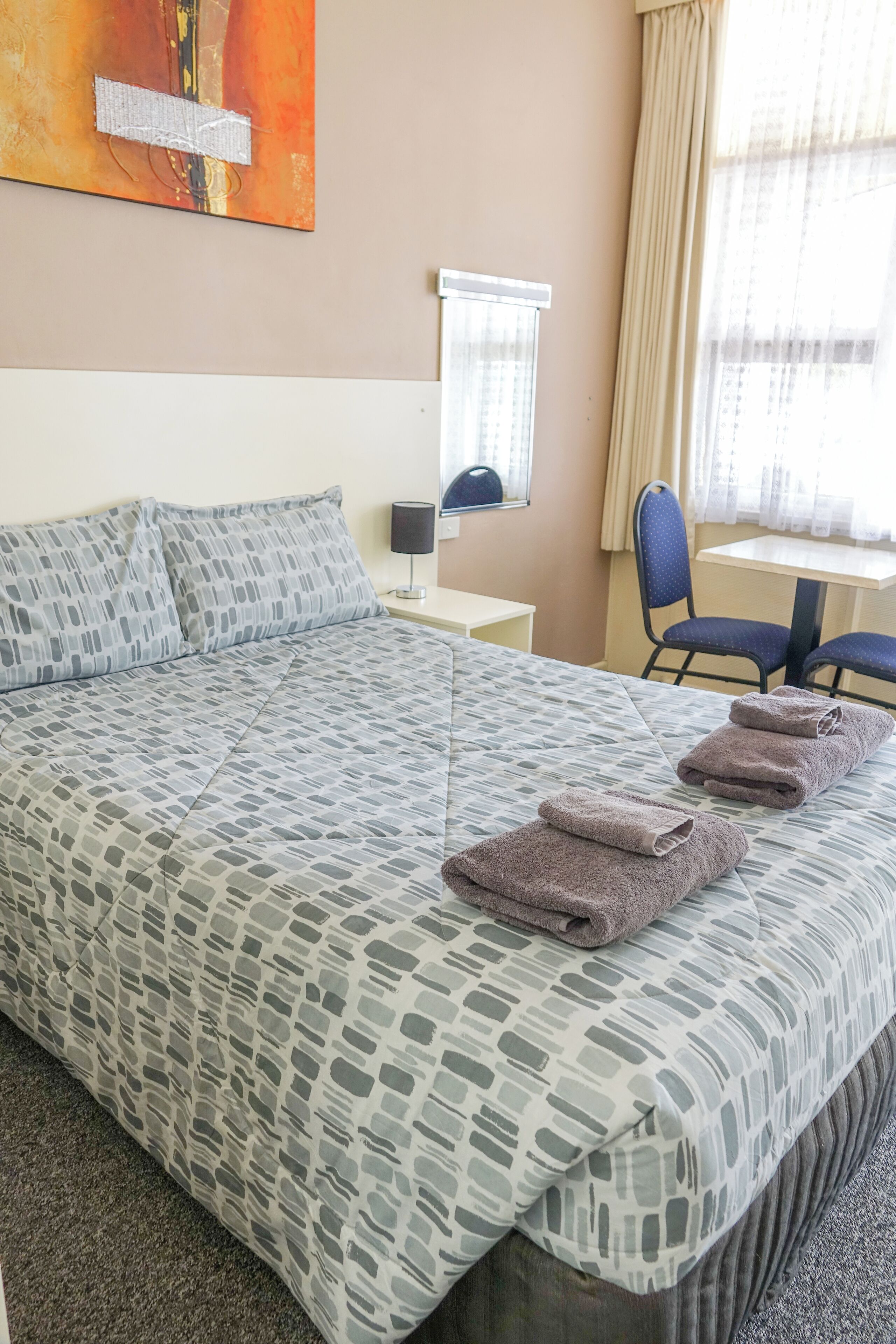 A hotel room with a large bed, a desk, a chair, and a painting on the wall.