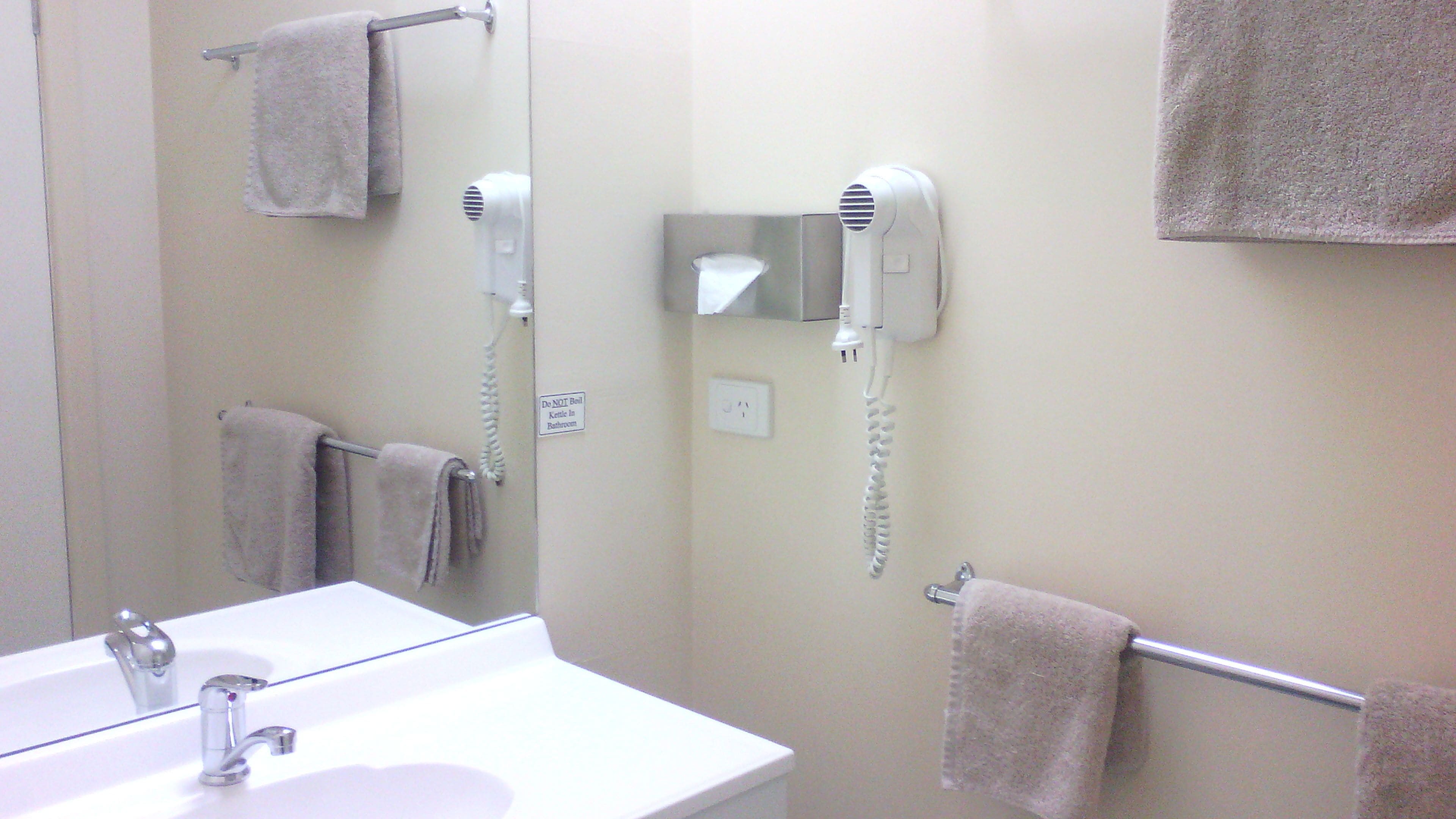 A bathroom with a sink, towel rack, hair dryer, and a sign prohibiting kettles.