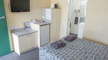 Quarto de hotel com uma cama, uma escrivaninha com computador, um mini frigorífico, uma televisão e um banheiro visível por uma porta aberta.