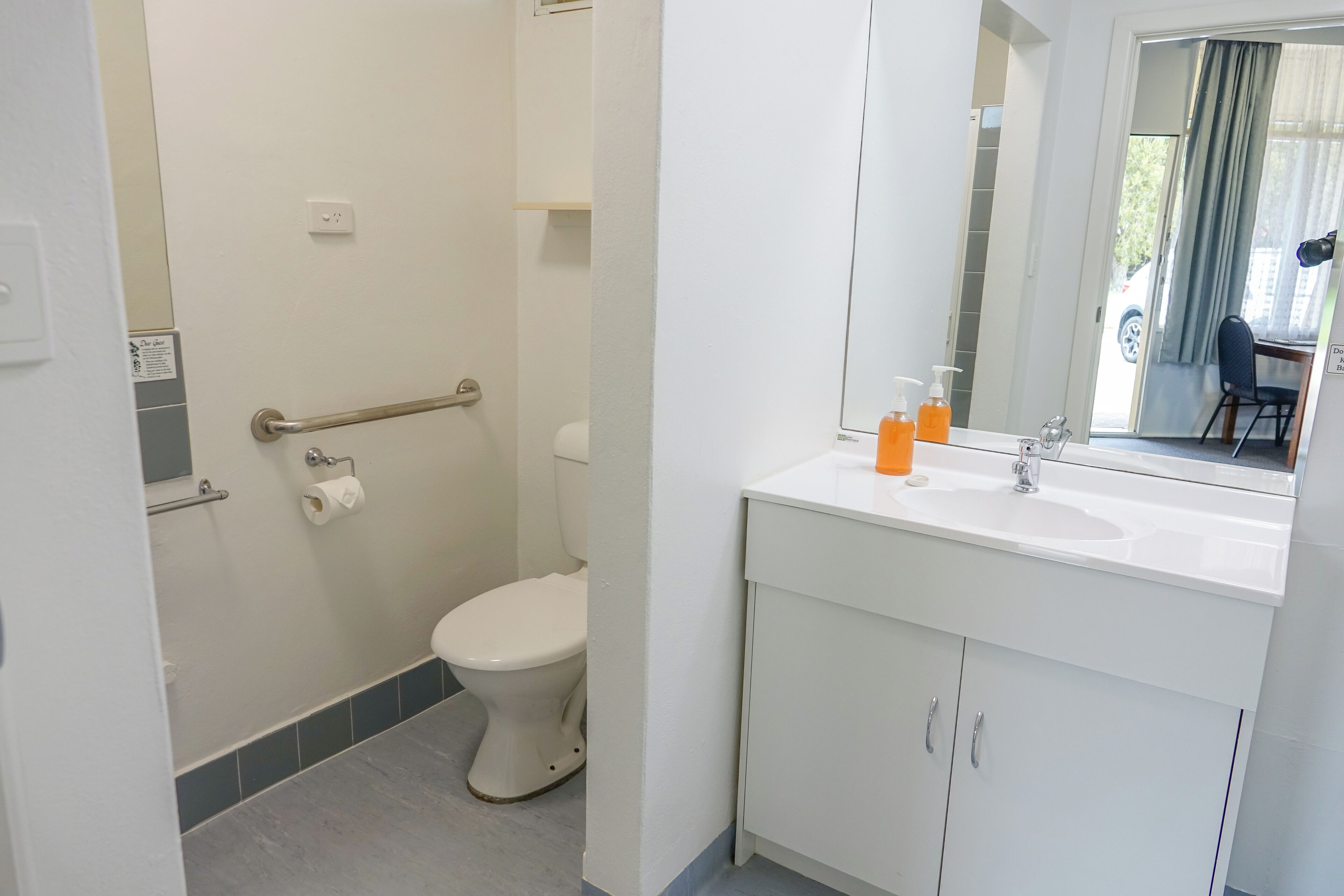 Un baño con inodoro, barra de apoyo, lavabo y espejo.