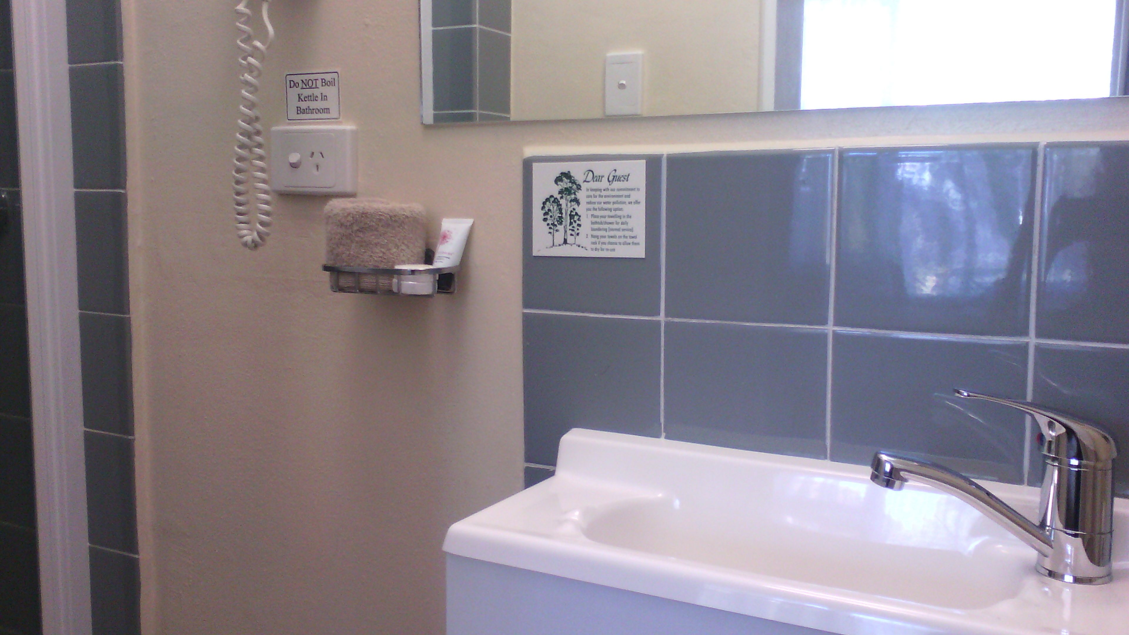 A bathroom with a sink, a towel rack, a sign advising not to boil kettles, and a guest message.