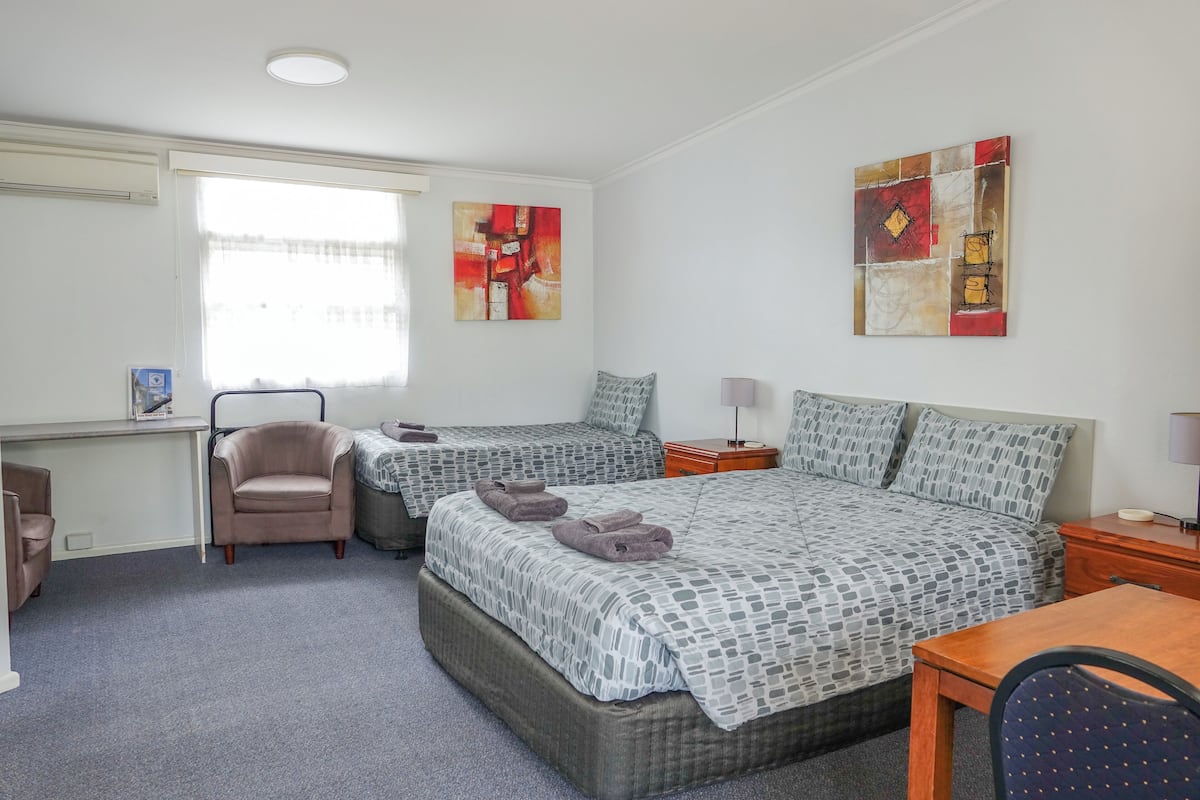 Une chambre d’hôtel avec deux lits, un bureau, une chaise et des œuvres d’art accrochées aux murs.