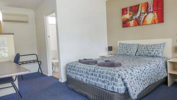 A hotel room with a bed, a desk, a chair, a bedside table, a lamp, and a painting on the wall.